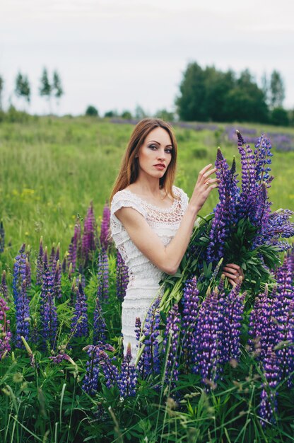 Ein Mädchen in einem weißen Kleid steht zwischen den Lupinen