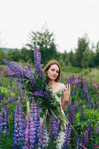 Ein Mädchen in einem weißen Kleid steht zwischen den Lupinen