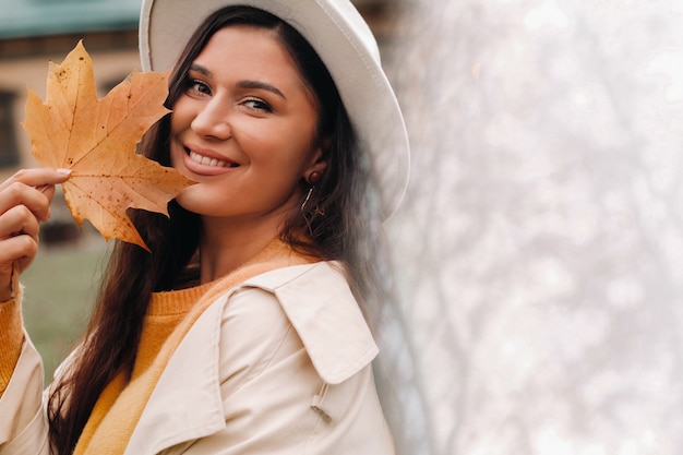 Ein Mädchen in einem weißen Mantel und Hut lächelt in einem Herbst Park.Portrait einer Frau im goldenen Herbst.