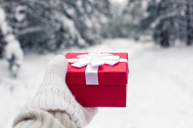 Foto ein mädchen in einem weißen pullover hält eine rote geschenkbox in weißem fäustling in der hand