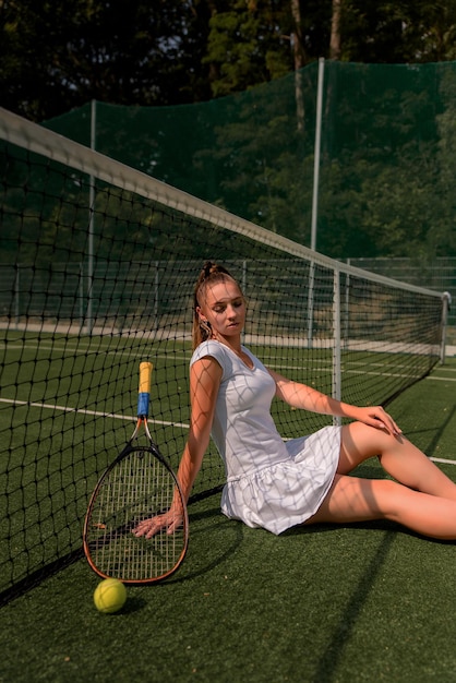 Ein Mädchen in einem weißen Sportkleid steht auf einem Tennisplatz und hält ein Schlägerporträt eines Mädchens auf dem Tennisplatz