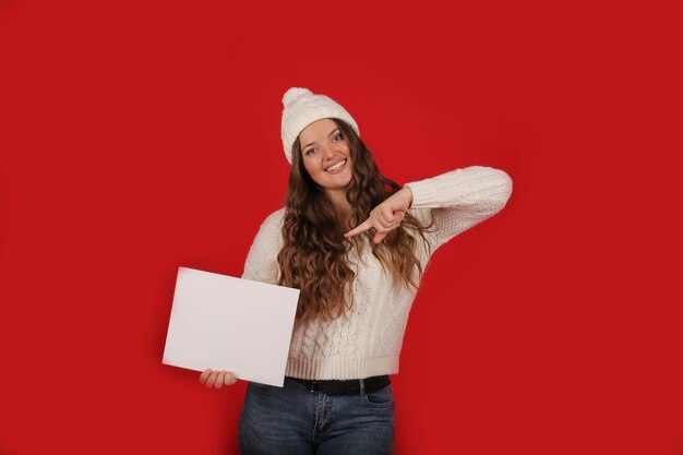 Ein Mädchen in einem weißen Strickpullover mit einer Wintermütze hält ein weißes Blatt Papier in den Händen