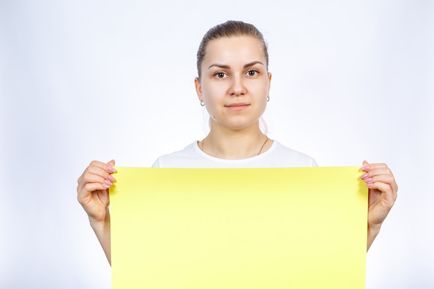 Foto ein mädchen in einem weißen t-shirt hält ein gelbes, leeres großes blatt banner.