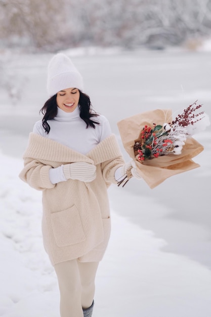 Ein Mädchen in einer beigen Strickjacke und Winterblumen geht in der Schneesaison in der Natur spazieren Winterwetter