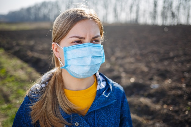 Ein Mädchen in einer blauen Jacke in der Natur setzt eine medizinische Schutzmaske auf. Sonniger Tag im Freien Maske im Gesicht vor Viren