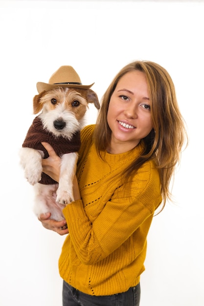 Ein Mädchen in einer gelben Jacke hält einen Jack Russell Terrier-Welpen in einem Cowboyhut. Auf weißem Hintergrund isolieren