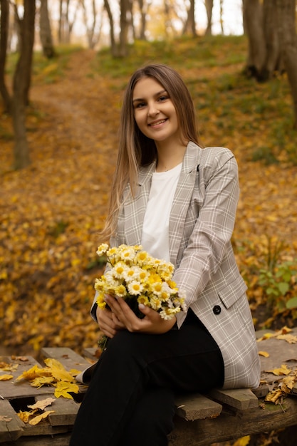 Ein Mädchen in einer grauen Jacke auf der Brücke hält einen Blumenstrauß im städtischen Herbstwald