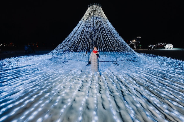 Ein Mädchen in einer grauen Jacke im Winter mit Abendlichtern, die auf der Weihnachtsstraße brennen.