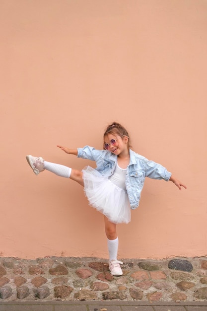 Ein Mädchen in einer Jeansjacke und einem weißen Rock hebt ihr Bein hoch in eine Pose