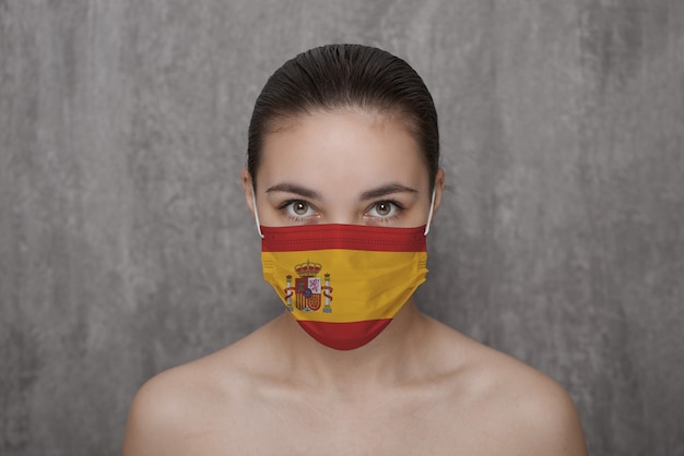 Ein Mädchen in einer Maske im Gesicht mit der Flagge des Landes Spanien