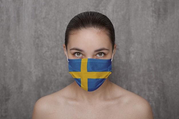 Ein Mädchen in einer Maske im Gesicht mit einer schwedischen Flagge