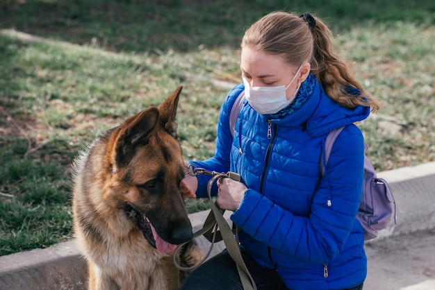 Ein Mädchen in einer medizinischen Schutzmaske geht mit einem Hund auf die Straße. Freizeit mit einem Haustier während der Quarantäne. Selbstisolations- und Schutzmodus.