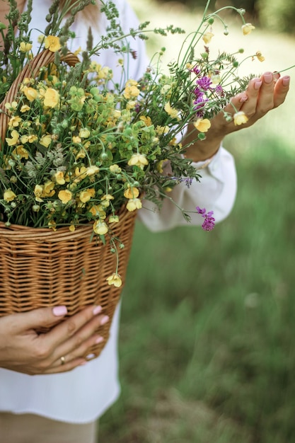 Ein Mädchen in einer weißen Bluse hält einen Weidenkorb mit einem Strauß wilder Blumen Sommerspaziergang im Mittelteil des Feldes