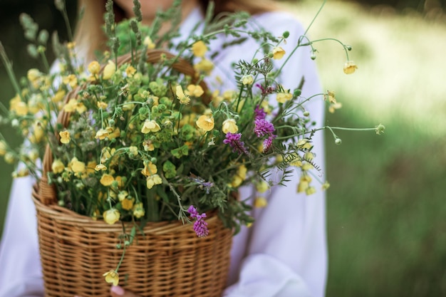 Ein Mädchen in einer weißen Bluse hält einen Weidenkorb mit einem Strauß wilder Blumen Sommerspaziergang im Mittelteil des Feldes