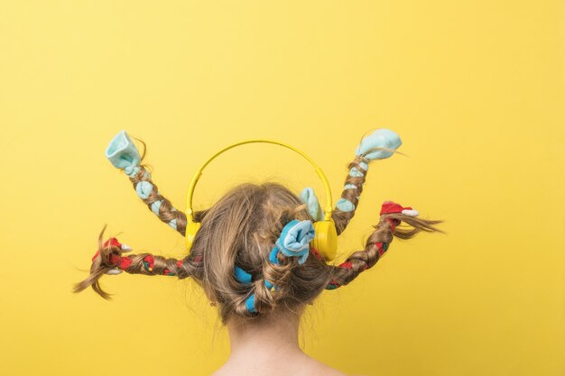 Ein Mädchen in gelben Kopfhörern mit fliegenden geflochtenen Haaren auf gelbem Grund. Eilen.