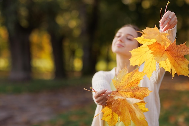 Ein Mädchen in gelber Kleidung in einem Herbstpark freut sich im Herbst und hält gelbe Blätter in ihren Händen