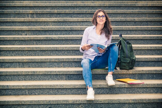 Ein Mädchen in Gläsern mit Büchern sitzt auf der Treppe