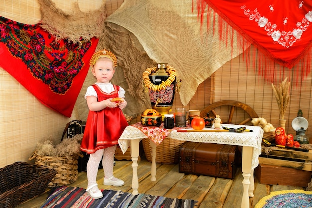 Ein Mädchen in roter Tracht neben einem Tisch mit Samowar und Lenkrädern Pfannkuchentag