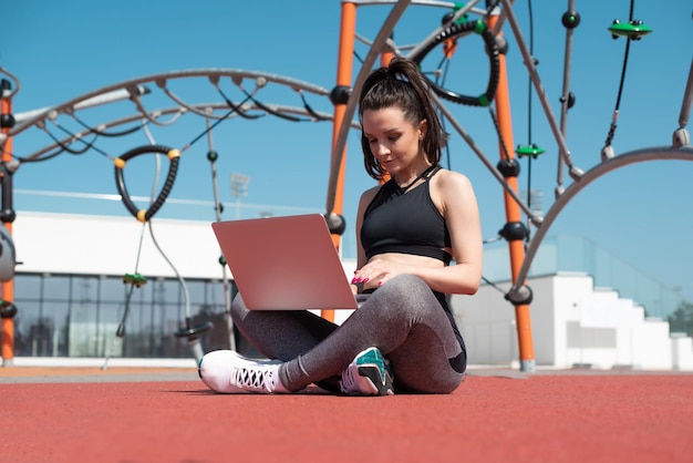 Ein Mädchen in Sportbekleidung auf einem Sommersportplatz im Freien sitzt mit einem Laptop