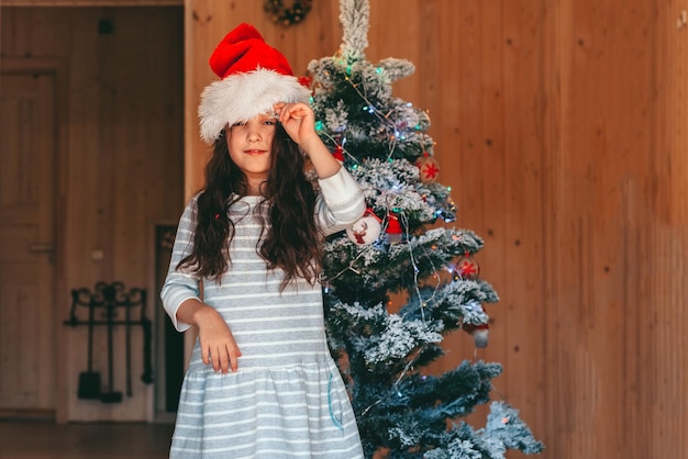 ein mädchen in weihnachtsmütze mit weihnachtsbaum zu hause