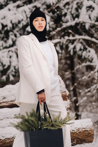 Foto ein mädchen in weißem anzug und sturmhaube mit einem paket weihnachtsbäume im winterwald an silvesterneujahrskonzept