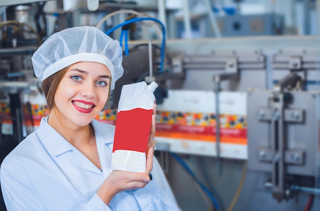 Ein Mädchen in weißen Overalls und einem Kopfschmuck in der Lebensmittelproduktion hält die Verpackung der Produkte in der Hand.