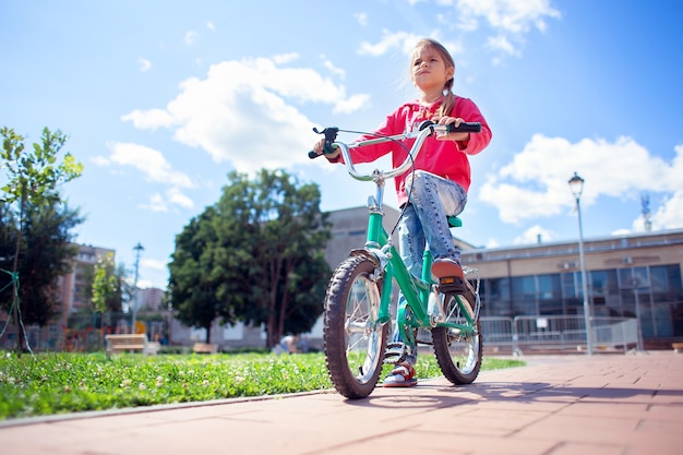 Ein Mädchen in zerrissenen Jeans fährt Fahrrad im Park.