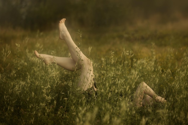 Ein Mädchen liegt auf dem Rücken im hohen grünen Gras Frauen nackte Füße hautnah Soft-Fokus