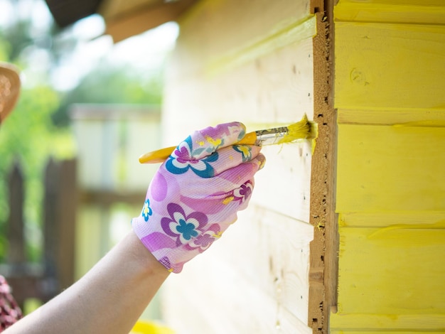 Ein Mädchen malt eine Holzwand mit einem Pinsel mit gelber Farbe