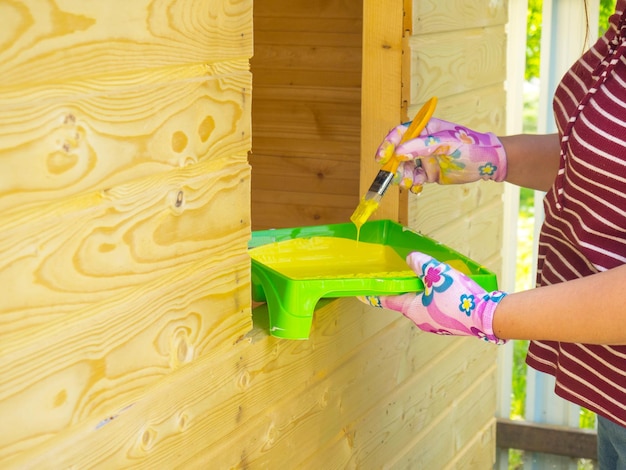 Ein Mädchen malt eine Holzwand mit einem Pinsel mit gelber Farbe