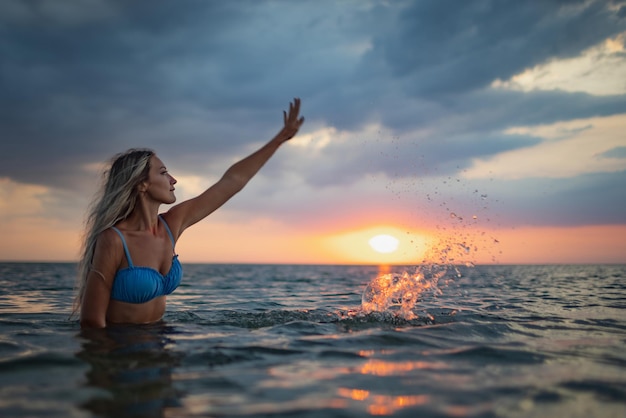 Ein Mädchen mit blonden Haaren in einem blauen Badeanzug spritzt an den Seiten, während es in einer Mündung auf einem Sonnenuntergangshintergrund sitzt