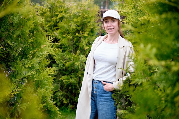 Ein Mädchen mit einem Lächeln im Gesicht in Jeans-Regenmantelmütze steht zwischen den grünen Büschen