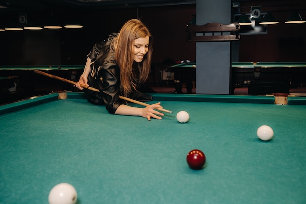 Ein Mädchen mit einem Queue in der Hand schießt auf einen Ball in einem Billardclub