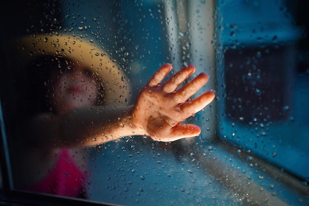 Ein Mädchen mit einem Strohhut regnet vor dem Fenster