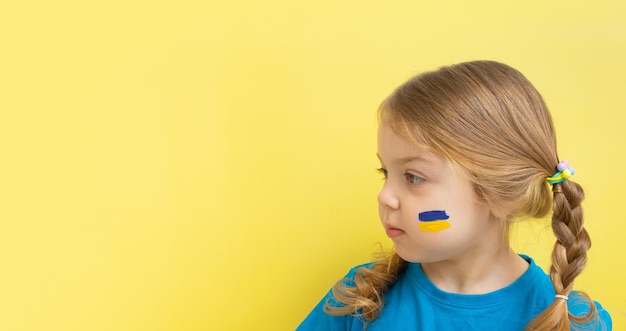 Ein Mädchen mit einer bemalten ukrainischen Flagge in Gelb und Blau auf ihren Wangen Kopieren Sie Platz auf gelbem Hintergrund