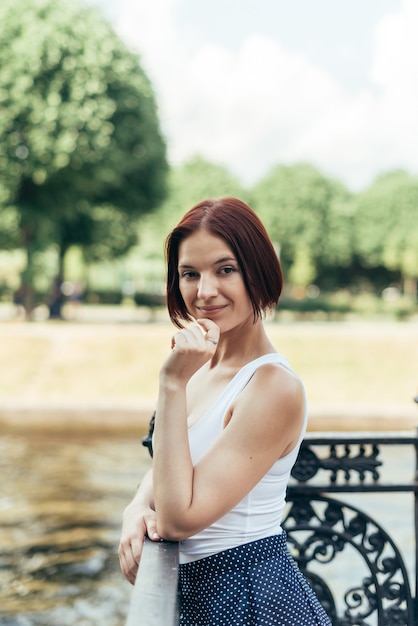 Ein Mädchen mit einer Bob-Frisur Kaukasier geht in einem Stadtpark auf der Brücke und schaut in die Kamera.