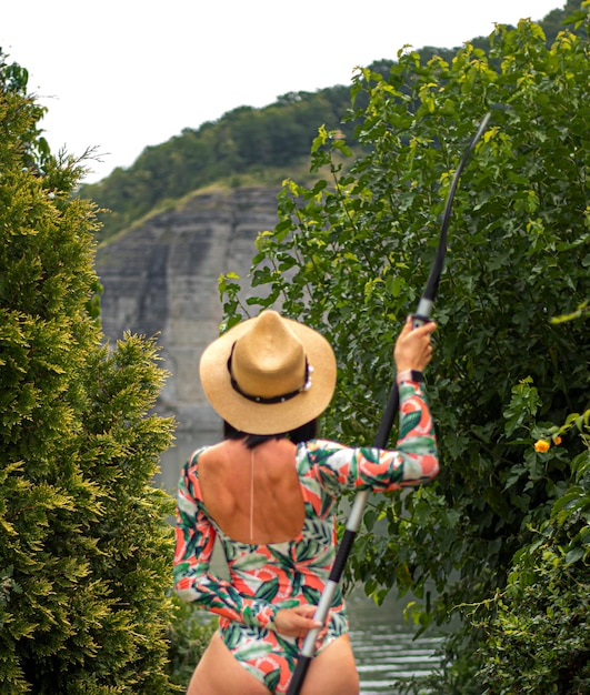 Ein Mädchen mit Hut und Ruder steht vor dem Hintergrund eines Flusses und Felsen. Ästhetisches Reisefoto