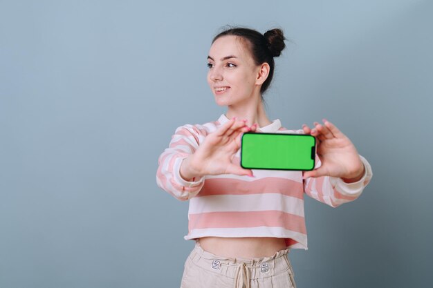 Ein Mädchen mit kindlicher Frisur hält ein Telefon mit grünem Bildschirm horizontal in den Händen und schaut weg