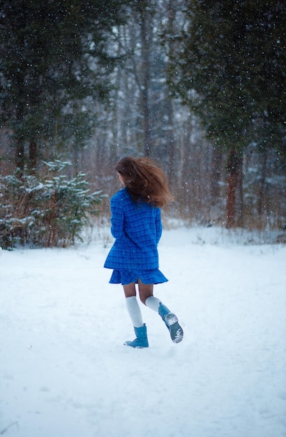 Foto ein mädchen mit langen haaren läuft in einem schneebedeckten wald in einem blauen anzug