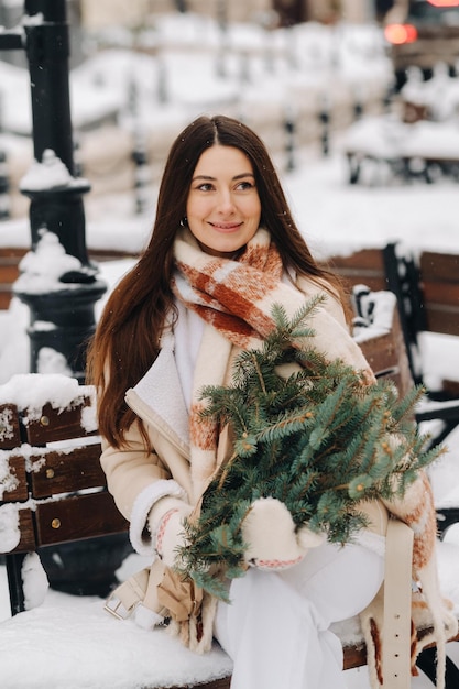 Ein Mädchen mit langen Haaren sitzt im Winter draußen auf einer Bank mit einem Strauß frischer Tannenzweige