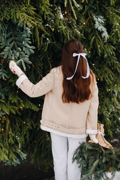 Ein Mädchen mit langen Haaren steht mit dem Rücken in einem Winterwald mit einem Strauß Tannenzweigen Verschneiter Winter