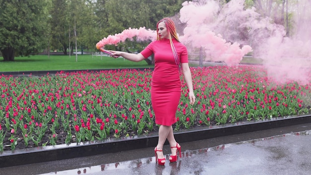 Ein Mädchen mit Make-up mit Regenbogenzöpfen im roten Kleid posiert im roten Kleid