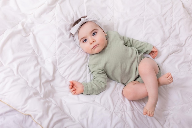 Ein Mädchen mit schönen großen Augen reibt das Baby zu Hause auf dem Bett in einem Baumwollbody auf weißer Bettwäsche