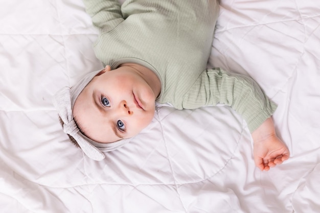 Ein Mädchen mit schönen großen Augen reibt das Baby zu Hause auf dem Bett in einem Baumwollbody auf weißer Bettwäsche