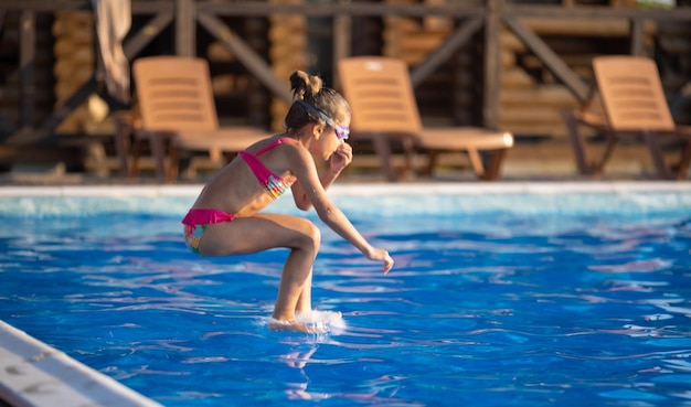 Ein Mädchen mit Schwimmbrille springt in einen Pool mit klarem Wasser auf dem Hintergrund eines warmen, sonnigen Sonnenuntergangs