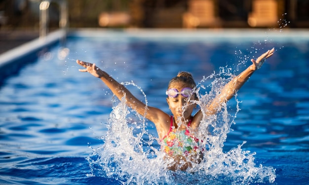 Ein Mädchen mit Schwimmbrille springt in einen Pool mit klarem Wasser auf dem Hintergrund eines warmen, sonnigen Sonnenuntergangs