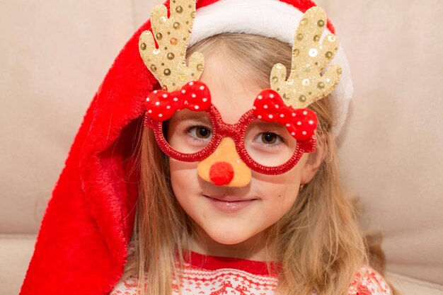 ein Mädchen mit Weihnachtsmannmütze und Weihnachtsbrille in Form von Weihnachtsbäumen