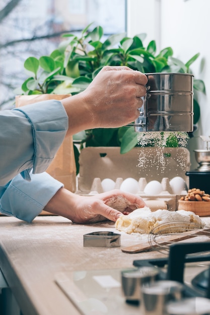 Ein Mädchen ohne Gesicht bereitet Teig vor, bestreut ihn mit Mehl, Nahaufnahme. Kochen hausgemachter Kuchen in der Küche zu Hause. Kulinarische Hintergründe.