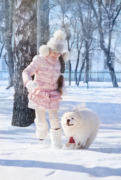 Ein Mädchen rennt und spielt mit einem Samojeden im Schnee,