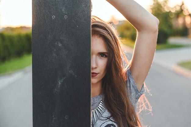 Ein Mädchen schaut aus dem Skateboard. stilvolles im Freienportrait eines schönen Brunettemädchens.